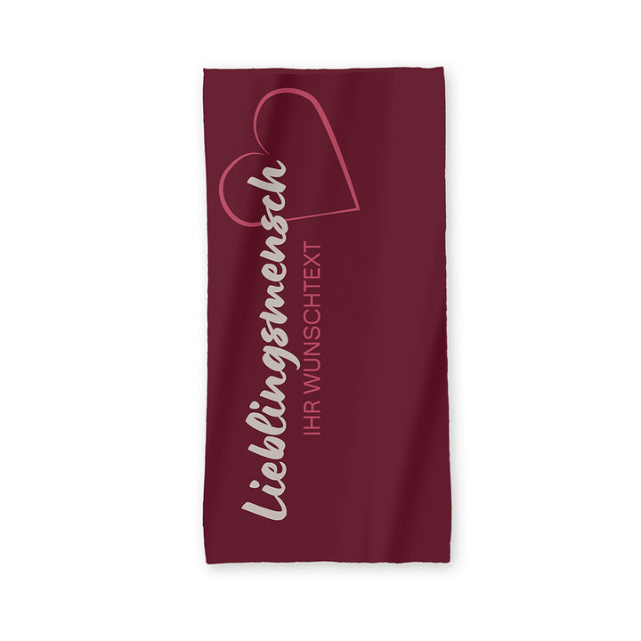 Der Hintergrund des Handtuchs ist in einem Bordeaux angelegt.
in einem hellen grau steht in geschwungener Schrift "Lieblingsmensch". Darunter ist in einem helleren Rot "Ihr Wunschtext" abgebildet.
Am Ende des Wortes "Lieblingsmensch!" ist ein Herz in einem hellen rot dargestellt.