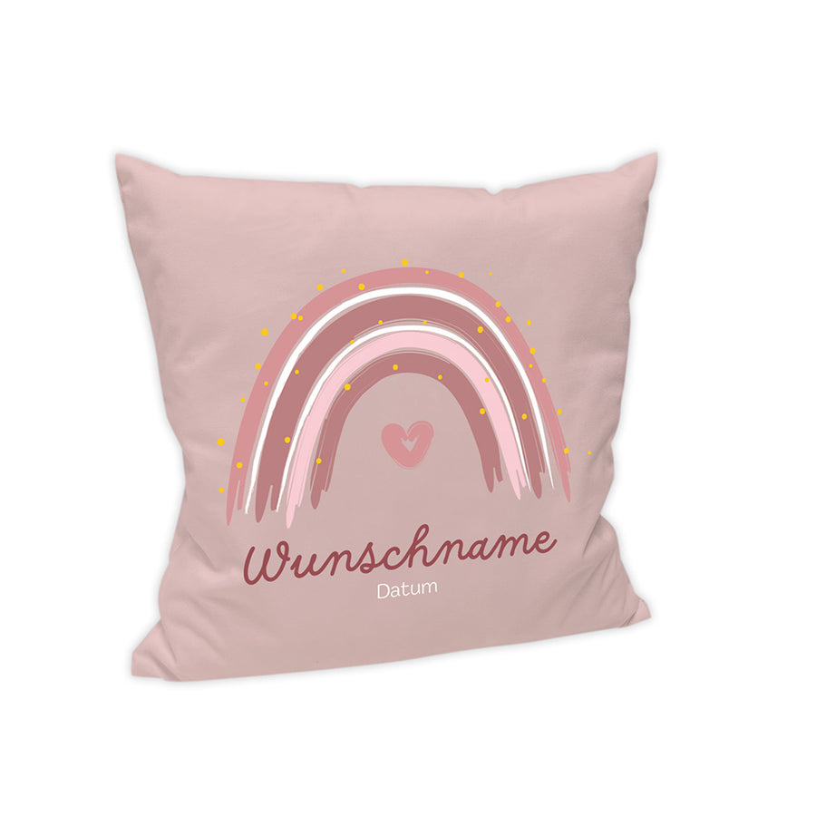 Das Kissen hat einen hellen rosa Hintergrund. Mittig ist ein abstrakter Regenbogen in Rosa Abstufungen dargestellt. Unterhalb des Bogens ist ein rosa Herz dargestellt. Unter dem Regenbogen steht in einer geschwungenen Schriftart "Wunschname" in einem Bordeaux. unterhalb des Wunschnames steht in einer Standardschrift "Datum" in Weiß.