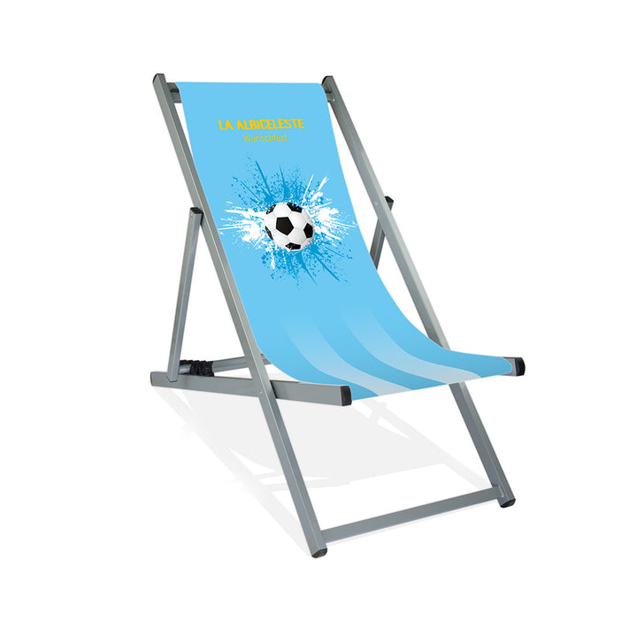 Aluminiumliegestuhl in Silber im Argentinien Design zur WM 2026 mit Fußball auf blau-weiß-blauen Farbklecks und personalisierbaren Text oberhalb. Über dem Wunschtext steht in gelb "La Albiceleste".
Der Hintergrund ist hellblau.