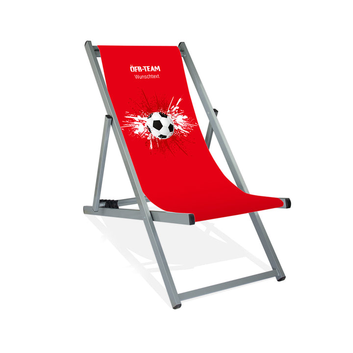 Aluminiumliegestuhl in Silber im Österreich Design zur WM 2026 mit Fußball auf rot-weiß-roten Farbklecks und personalisierbaren Text oberhalb. Über dem Wunschtext steht in weiß "ÖFB-Team".
Der Hintergrund ist rot.