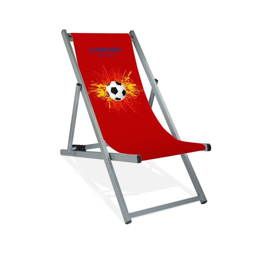 Aluminiumliegestuhl in Silber im Spanien Design zur WM 2026 mit Fußball auf rot-gelb-roten Farbklecks und personalisierbaren Text oberhalb. Über dem Wunschtext steht in blau "La Furia Roja".
Der Hintergrund ist rot.