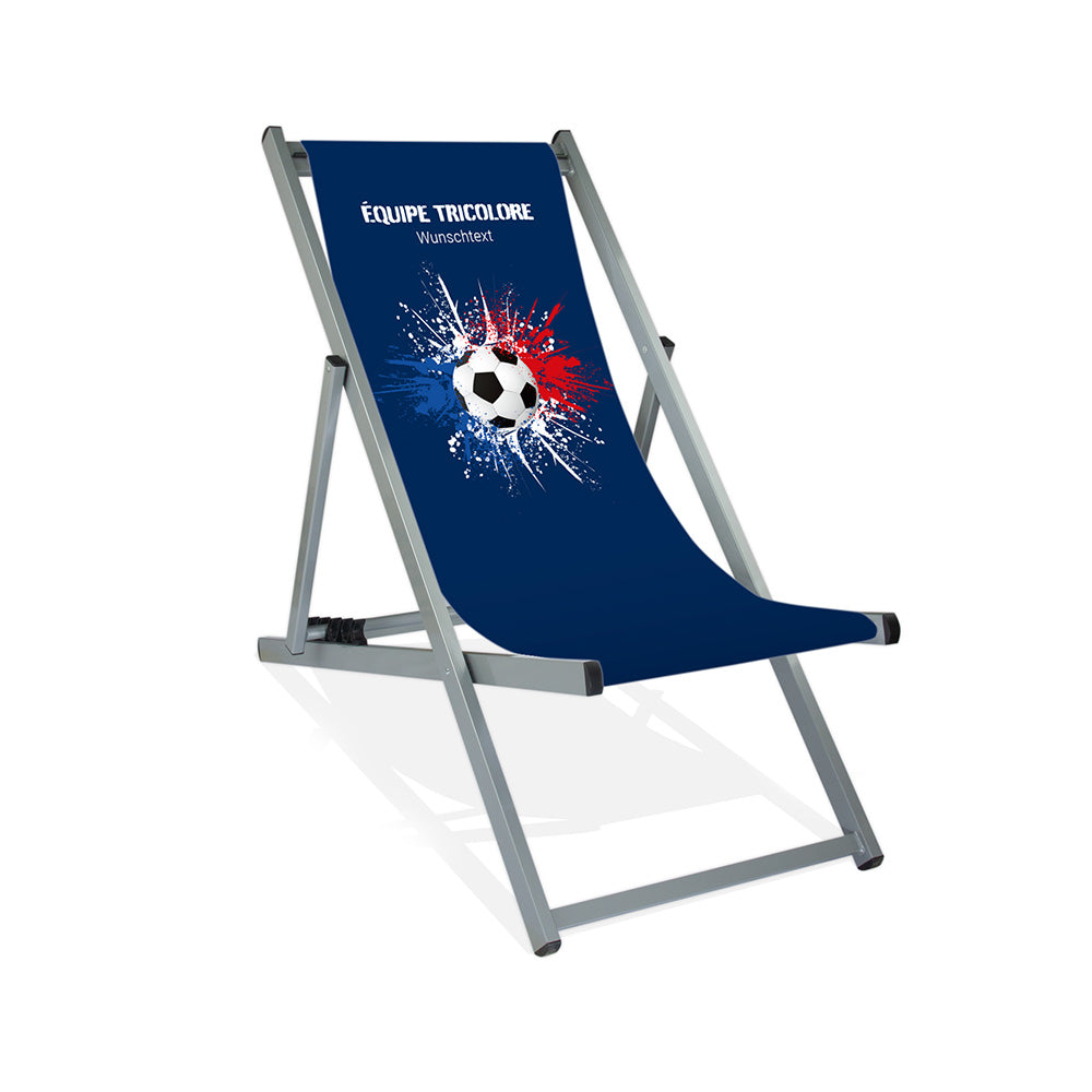 Aluminiumliegestuhl in Silber im Frankreich Design zur WM 2026 mit Fußball auf blau-weiß-roten Farbklecks und personalisierbaren Text oberhalb. Über dem Wunschtext steht in weiß "Equipe Tricolore".
Der Hintergrund ist blau.
