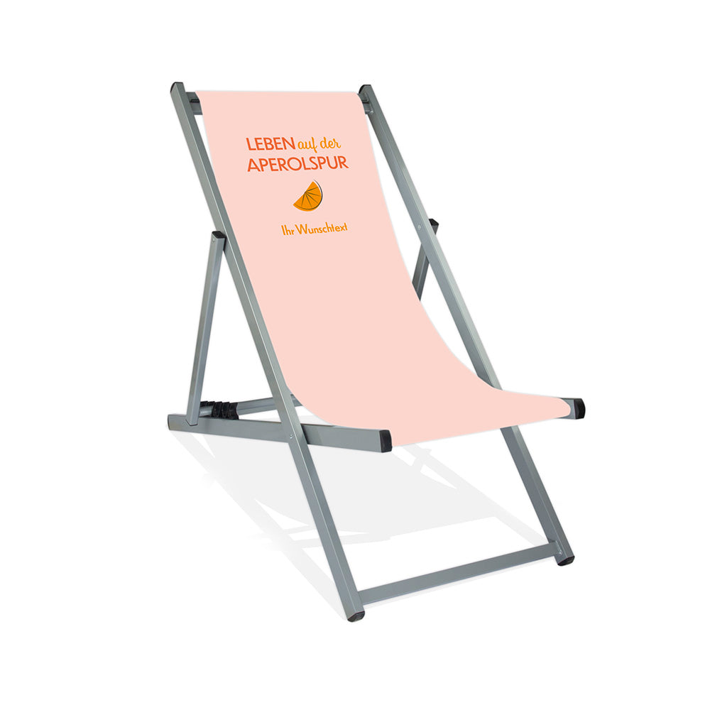 Mittig ist ein silber Alumiumliegestuhl ohne Armlehne abgebildet.
Helles Motiv mit dem Spruch "Leben auf der Aperolspur". 