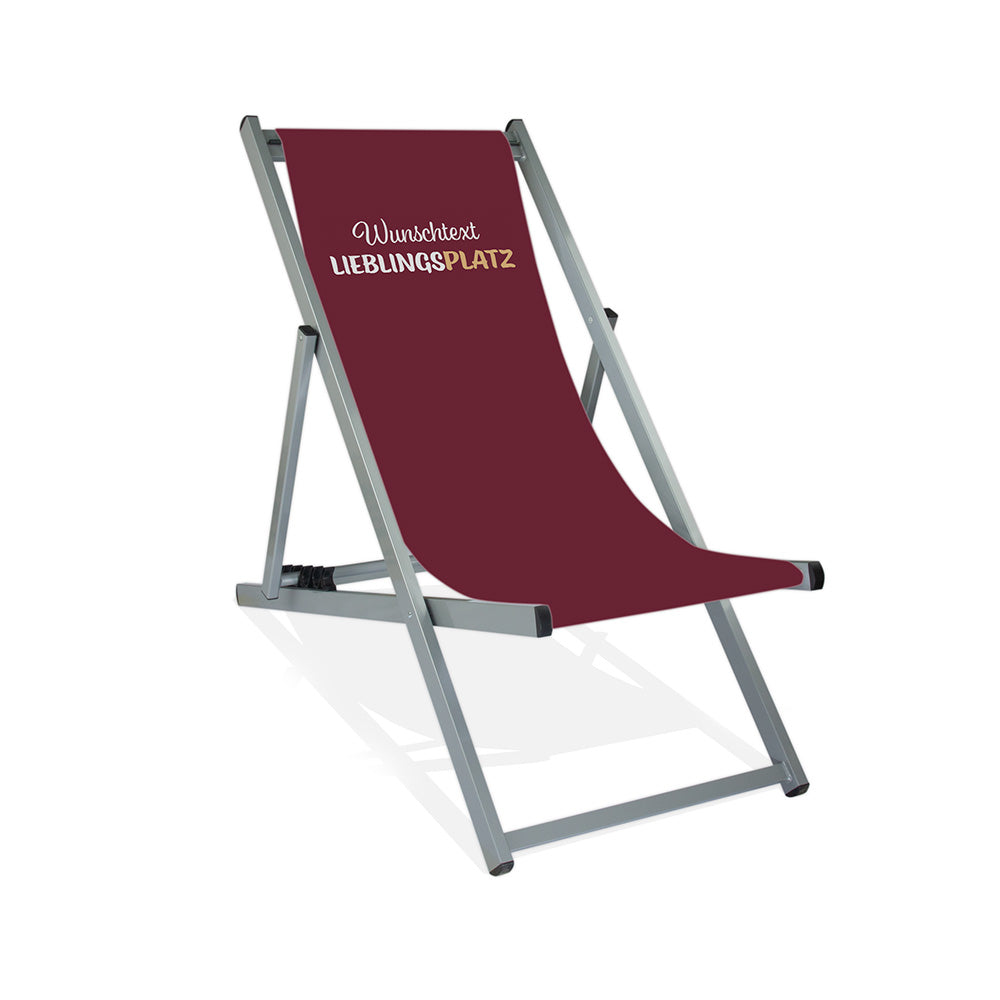 Mittig Aluminium-Liegestuhl in Silber Lasur. Das Motiv besitzt einen  Hintergrund in beere. Im oberen Bereich ist der Text "Wunschtext" und darunter "LIEBLINGSPLATZ" abgebildet.