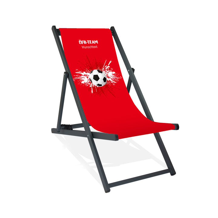 Aluminiumliegestuhl in Schwarz im Österreich Design zur WM 2026 mit Fußball auf rot-weiß-roten Farbklecks und personalisierbaren Text oberhalb. Über dem Wunschtext steht in weiß "ÖFB-Team".
Der Hintergrund ist rot.