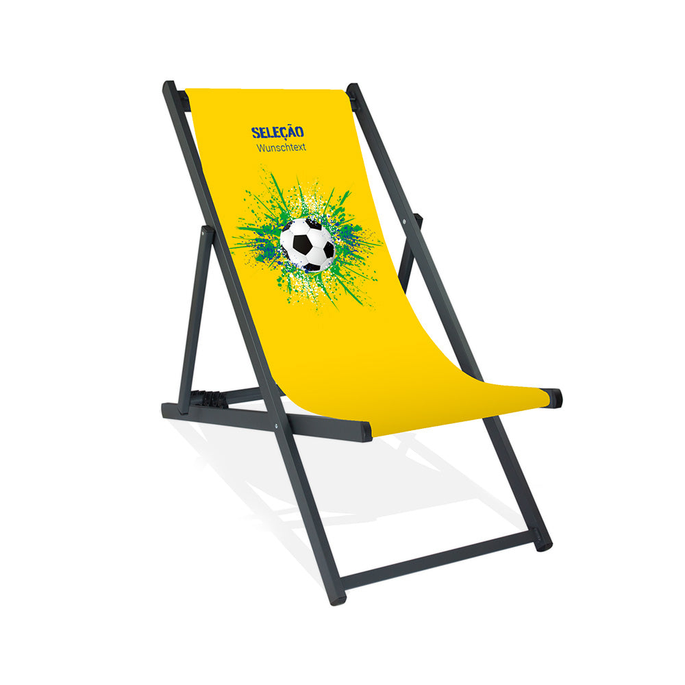 Aluminiumliegestuhl in Schwarz im Brasilien Design zur WM 2026 mit Fußball auf grün-blau-weißen Farbklecks und personalisierbaren Text oberhalb. Über dem Wunschtext steht in blau "Selecao".
Der Hintergrund ist gelb.