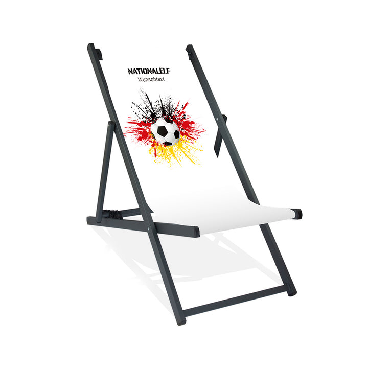 Aluminiumliegestuhl in Schwarz im Deutschland Design zur WM 2026 mit Fußball auf schwarz-rot-goldenem Farbklecks und personalisierbaren Text oberhalb. Über dem Wunschtext steht "Nationalelf"