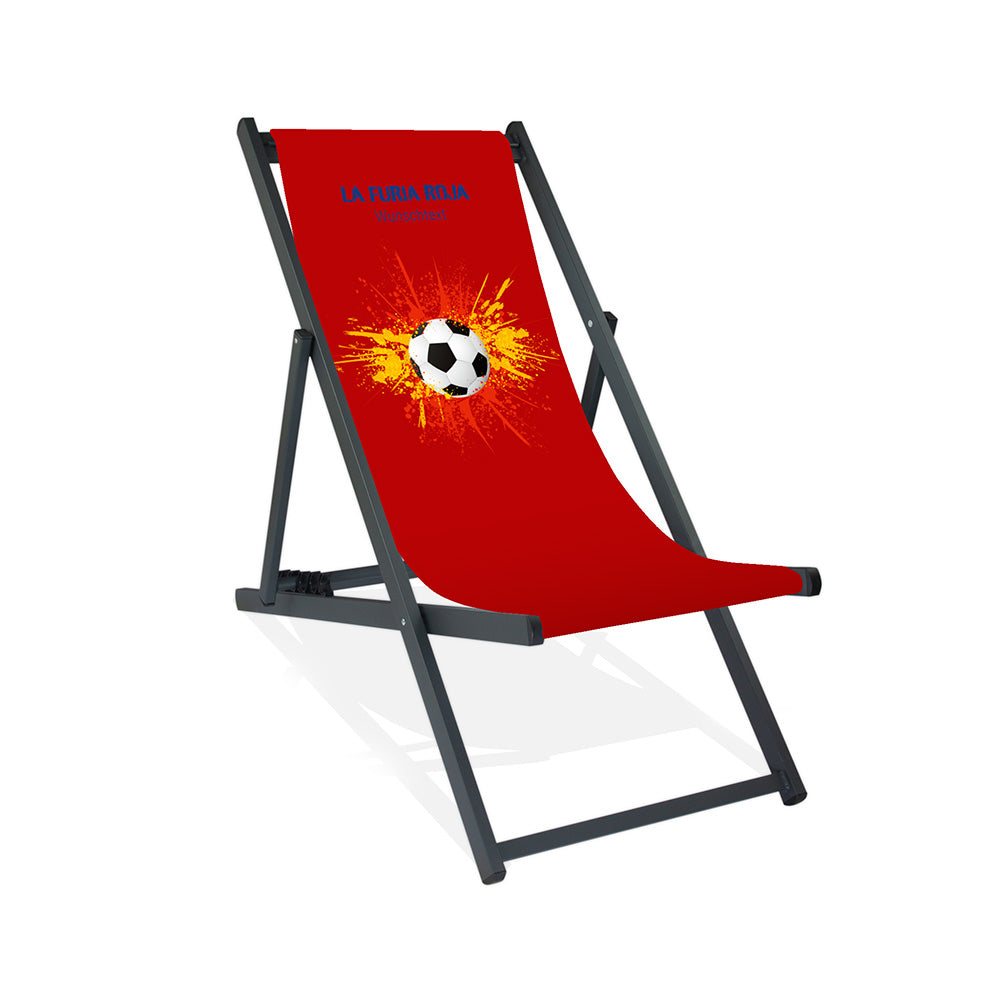 Aluminiumliegestuhl in Schwarz im Spanien Design zur WM 2026 mit Fußball auf rot-gelb-roten Farbklecks und personalisierbaren Text oberhalb. Über dem Wunschtext steht in blau "La Furia Roja".
Der Hintergrund ist rot.