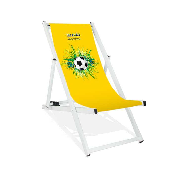 Aluminiumliegestuhl in Weiß im Brasilien Design zur WM 2026 mit Fußball auf grün-blau-weißen Farbklecks und personalisierbaren Text oberhalb. Über dem Wunschtext steht in blau "Selecao".
Der Hintergrund ist gelb.