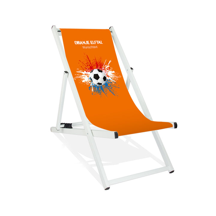 Aluminiumliegestuhl in Weiß im Niederlande Design zur WM 2026 mit Fußball auf rot-weiß-blauen Farbklecks und personalisierbaren Text oberhalb. Über dem Wunschtext steht "Oranje Elftal". Der Hintergrund ist orange.