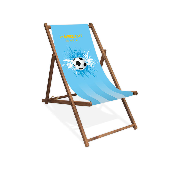 Liegestuhl ohne Armlehne dunkelbraun im Argentinien Design zur WM 2026 mit Fußball auf blau-weiß-blauen Farbklecks und personalisierbaren Text oberhalb. Über dem Wunschtext steht in gelb "La Albiceleste".
Der Hintergrund ist hellblau.
