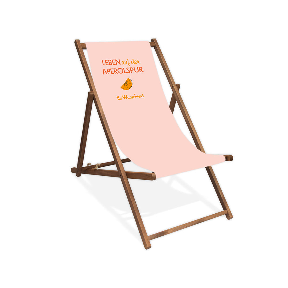 Mittig ist ein dunkelbrauner Holzliegestuhl ohne Armlehne abgebildet.
Helles Motiv mit dem Spruch "Leben auf der Aperolspur". 
