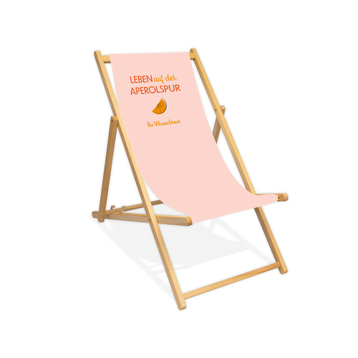 Mittig ist ein farbloser Holzliegestuhl ohne Armlehne abgebildet.
Helles Motiv mit dem Spruch "Leben auf der Aperolspur". 