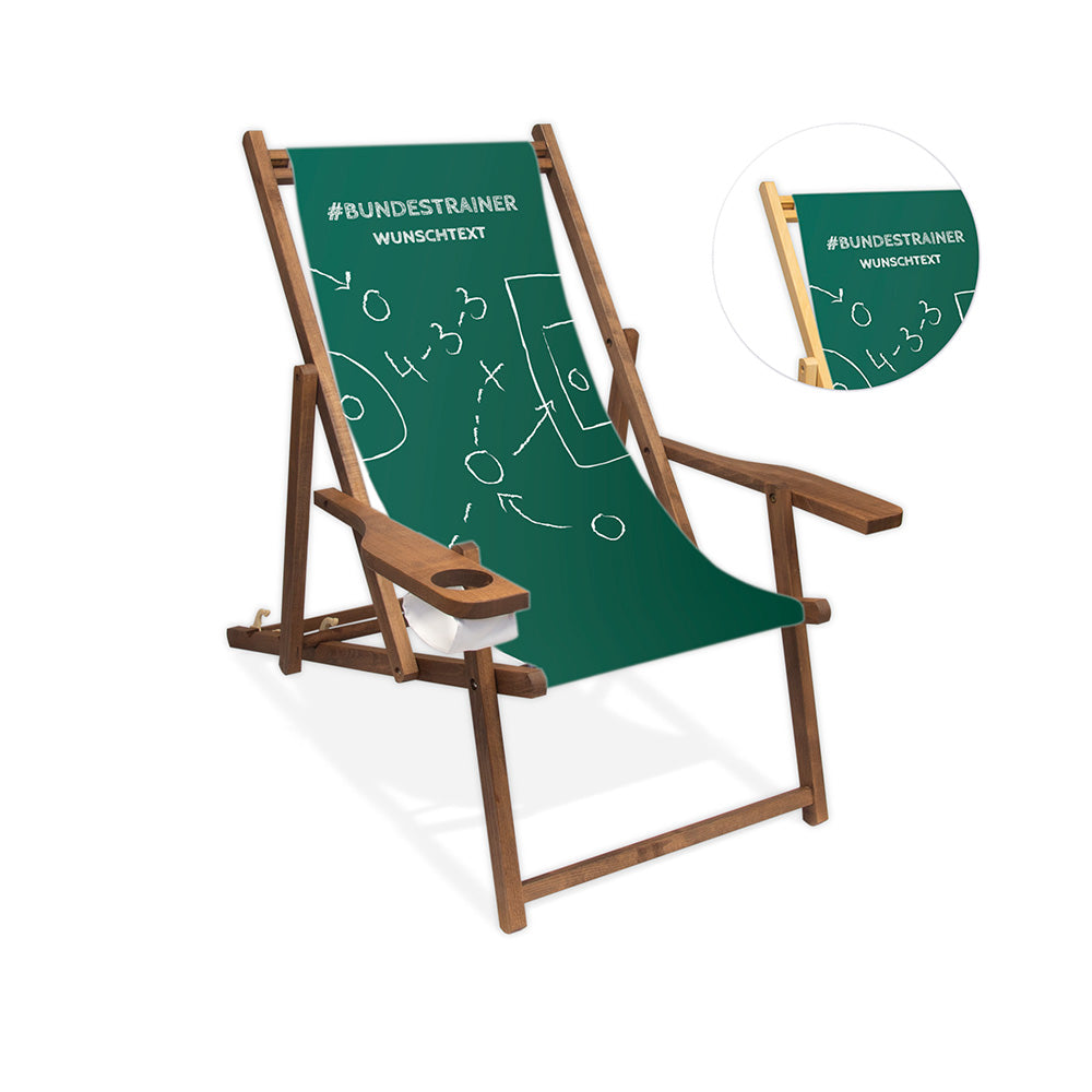 Liegestuhl mit Armlehne im Fußball Taktiktafel-Design mit grünem Hintergrund, Schriftzug "#Bundestrainer" und personalisierbarem Wunschtext. Die Lasur des Stuhls ist dunkelbraun.
Neben dem Stuhl ist in einem Kreis die Lasurfarbe farblos abgebildet.