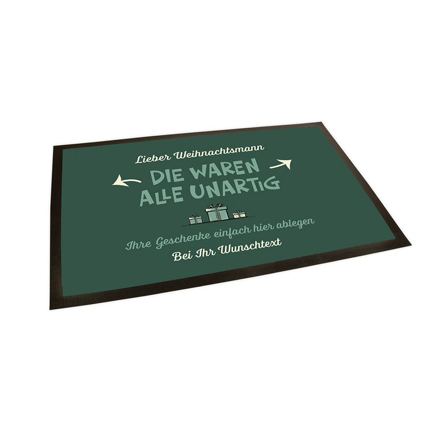 Der Hintergrund der Fußmatte ist in einem grün gehalten. Im oberen Bereich steht in einem Cremeton "Lieber Weihnachtsmann". Darunter steht in einem Mintton in einer Akzentschriftart "DIE WAREN ALLE UNARTIG". Von diesem Text aus gehen Pfeile nach links und rechts.
Darunter sind drei Geschenke abgebildet und darunter steht der Text "Ihre Geschenke einfach hier ablegen" "Bei Ihr Wunschtext".