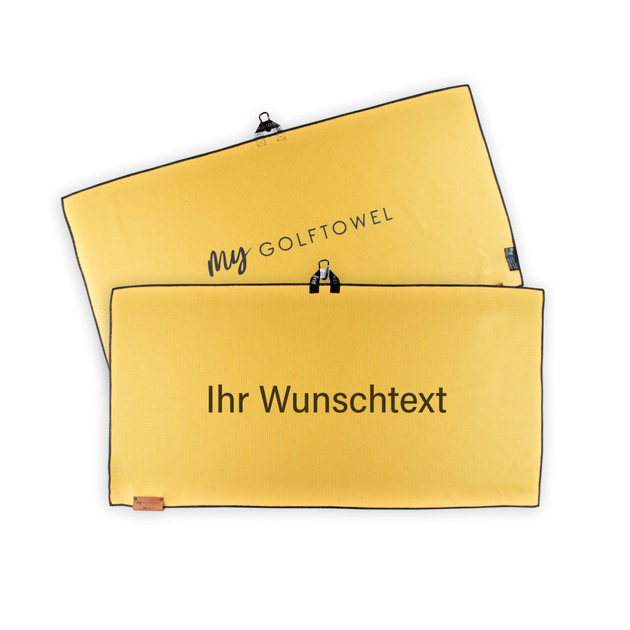 Golftowel Large in Gelb. Auf dem Golftowel steht Mittig in einer schwarzen, serifenlosen Schrift geschrieben "Ihr Wunschtext". Die Rückseite des Golftowels ist im gleichen Gelb, wie die Vorderseite dargestellt. Hier steht mittig der Schriftzug "MyGolftowel". Im unteren Bereich befindet sich ein braunes Lederpatch und oben ist eine Schlaufe und Karabiner angebracht.