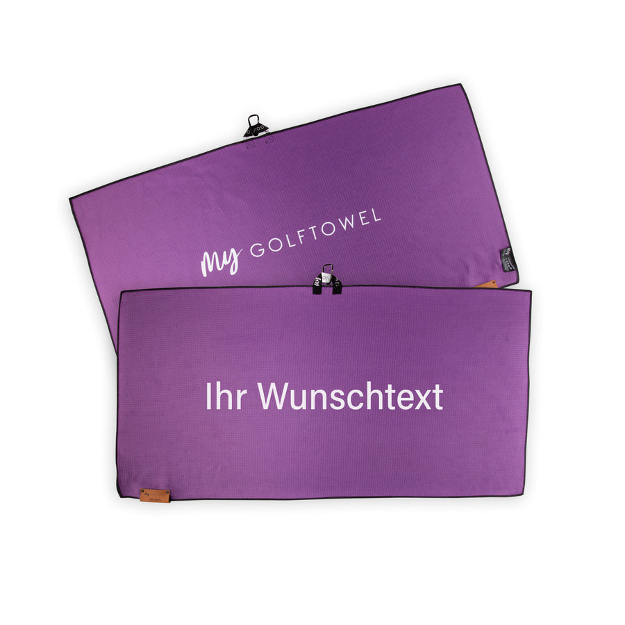 Golftowel Large in Lila. Auf dem Golftowel steht Mittig in einer weißen, serifenlosen Schrift geschrieben "Ihr Wunschtext". Die Rückseite des Golftowels ist im gleichen Lila, wie die Vorderseite dargestellt. Hier steht mittig der Schriftzug "MyGolftowel". Im unteren Bereich befindet sich ein braunes Lederpatch und oben ist eine Schlaufe und Karabiner angebracht.