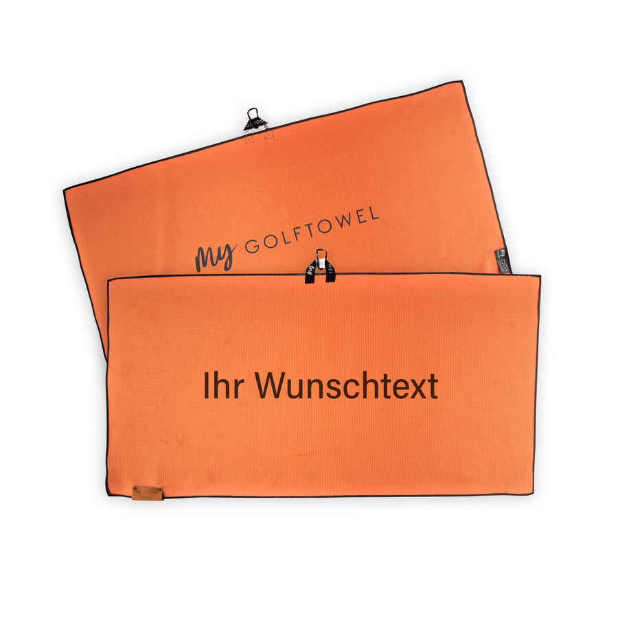 Golftowel Large in Orange. Auf dem Golftowel steht Mittig in einer schwarzen, serifenlosen Schrift geschrieben "Ihr Wunschtext". Die Rückseite des Golftowels ist im gleichen Orange, wie die Vorderseite dargestellt. Hier steht mittig der Schriftzug "MyGolftowel". Im unteren Bereich befindet sich ein braunes Lederpatch und oben ist eine Schlaufe und Karabiner angebracht.