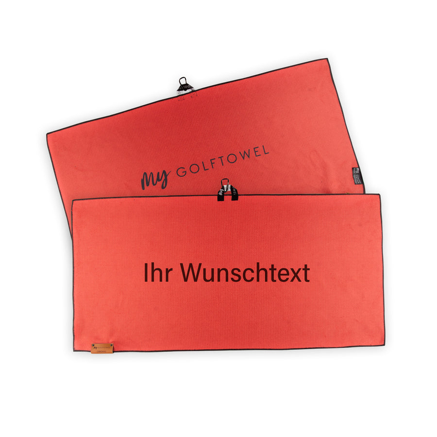 Golftowel Large in Rot. Auf dem Golftowel steht Mittig in einer weißen, serifenlosen Schrift geschrieben "Ihr Wunschtext". Die Rückseite des Golftowels ist im gleichen Rot, wie die Vorderseite dargestellt. Hier steht mittig der Schriftzug "MyGolftowel". Im unteren Bereich befindet sich ein braunes Lederpatch und oben ist eine Schlaufe und Karabiner angebracht.