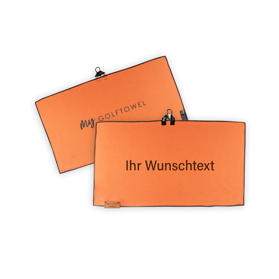 Golftowel Medium in Orange. Auf dem Golftowel steht Mittig in einer schwarzen, serifenlosen Schrift geschrieben "Ihr Wunschtext". Die Rückseite des Golftowels ist im gleichen Orange, wie die Vorderseite dargestellt. Hier steht mittig der Schriftzug "MyGolftowel". Im unteren Bereich befindet sich ein braunes Lederpatch und oben ist eine Schlaufe und Karabiner angebracht.