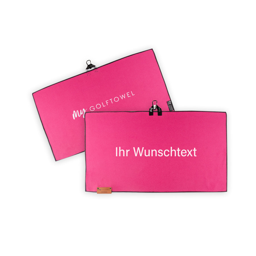 Golftowel Medium in Pink. Auf dem Golftowel steht Mittig in einer weißen, serifenlosen Schrift geschrieben "Ihr Wunschtext". Die Rückseite des Golftowels ist im gleichen Pink, wie die Vorderseite dargestellt. Hier steht mittig der Schriftzug "MyGolftowel". Im unteren Bereich befindet sich ein braunes Lederpatch und oben ist eine Schlaufe und Karabiner angebracht.
