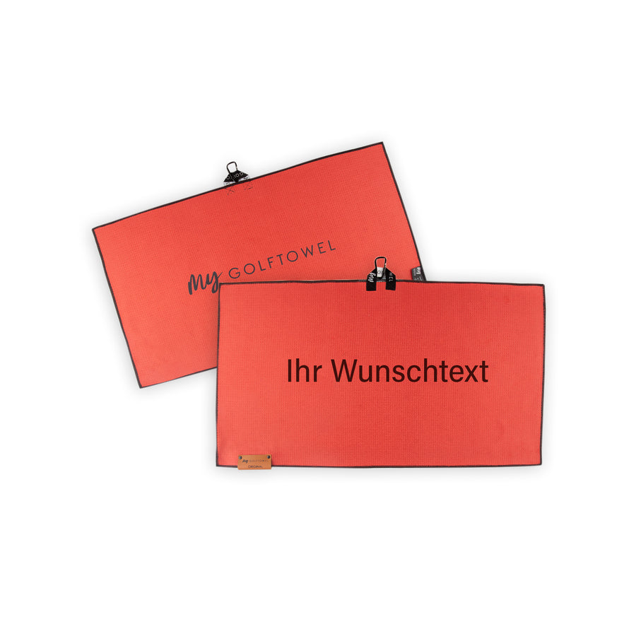 Golftowel Medium in Rot. Auf dem Golftowel steht Mittig in einer weißen, serifenlosen Schrift geschrieben "Ihr Wunschtext". Die Rückseite des Golftowels ist im gleichen Rot, wie die Vorderseite dargestellt. Hier steht mittig der Schriftzug "MyGolftowel". Im unteren Bereich befindet sich ein braunes Lederpatch und oben ist eine Schlaufe und Karabiner angebracht.