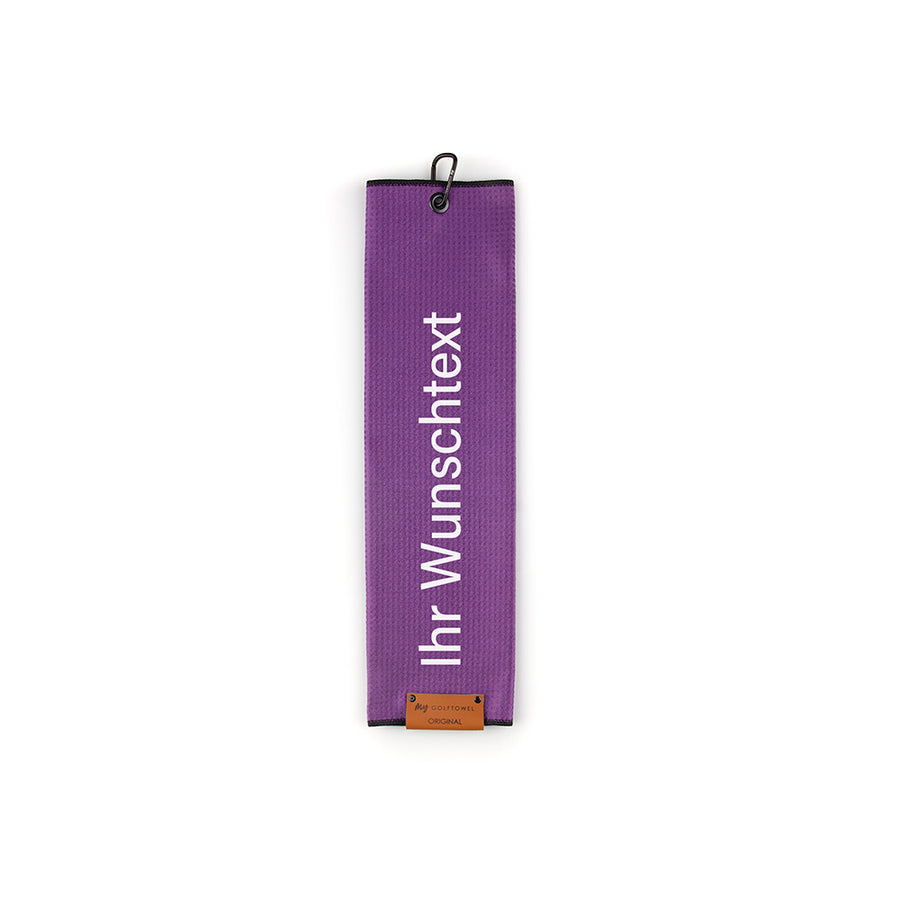 Gefaltetes Golftowel in Lila. Auf dem Golftowel steht von unten nach oben geschrieben der Text "Ihr Wunschtext" in Weiß. Im unteren Bereich befindet sich ein braunes Lederpatch und oben ist ein schwarzer Karabiner in einer schwarzen Öse angebracht.