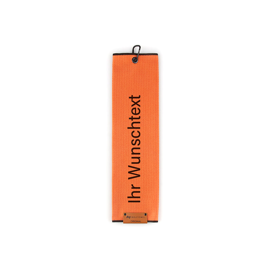 Gefaltetes Golftowel in Orange. Auf dem Golftowel steht von unten nach oben geschrieben der Text "Ihr Wunschtext" in Schwarz. Im unteren Bereich befindet sich ein braunes Lederpatch und oben ist ein schwarzer Karabiner in einer schwarzen Öse angebracht.