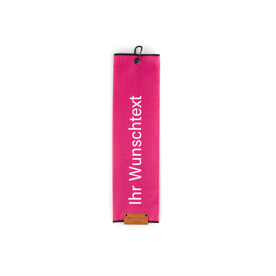 Gefaltetes Golftowel in Pink. Auf dem Golftowel steht von unten nach oben geschrieben der Text "Ihr Wunschtext" in Weiß. Im unteren Bereich befindet sich ein braunes Lederpatch und oben ist ein schwarzer Karabiner in einer schwarzen Öse angebracht.