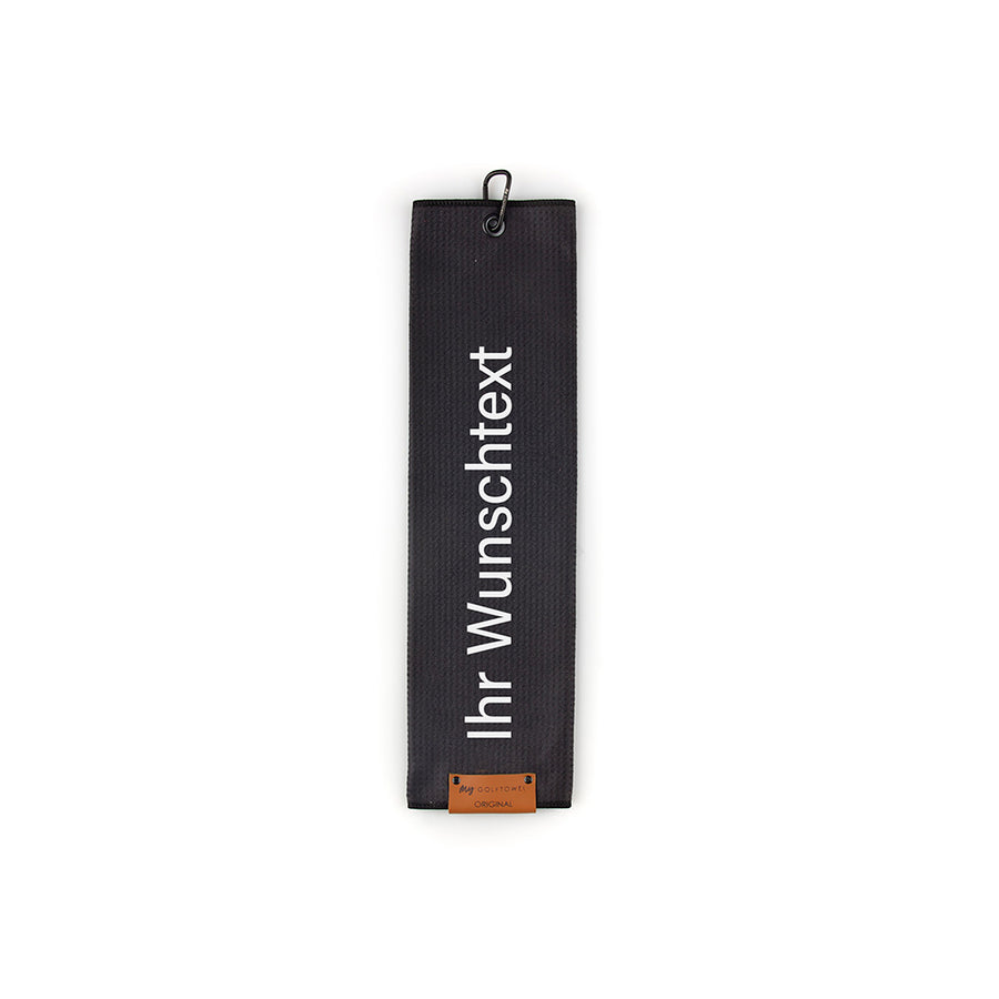 Gefaltetes Golftowel in Schwarz. Auf dem Golftowel steht von unten nach oben geschrieben der Text "Ihr Wunschtext" in Weiß. Im unteren Bereich befindet sich ein braunes Lederpatch und oben ist ein schwarzer Karabiner in einer schwarzen Öse angebracht.
