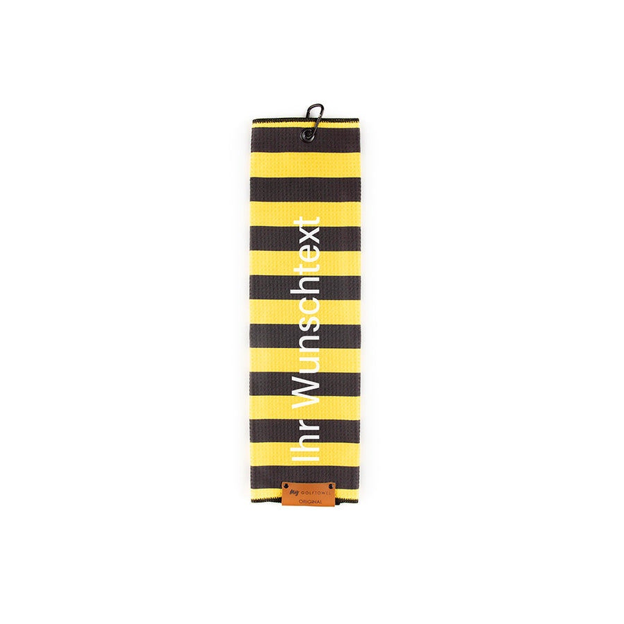 Gefaltetes Golftowel mit horizontalen Streifen in Gelb-Schwarz. Auf dem Golftowel steht von unten nach oben geschrieben der Text "Ihr Wunschtext" in Weiß. Im unteren Bereich befindet sich ein braunes Lederpatch und oben ist ein schwarzer Karabiner in einer schwarzen Öse angebracht.