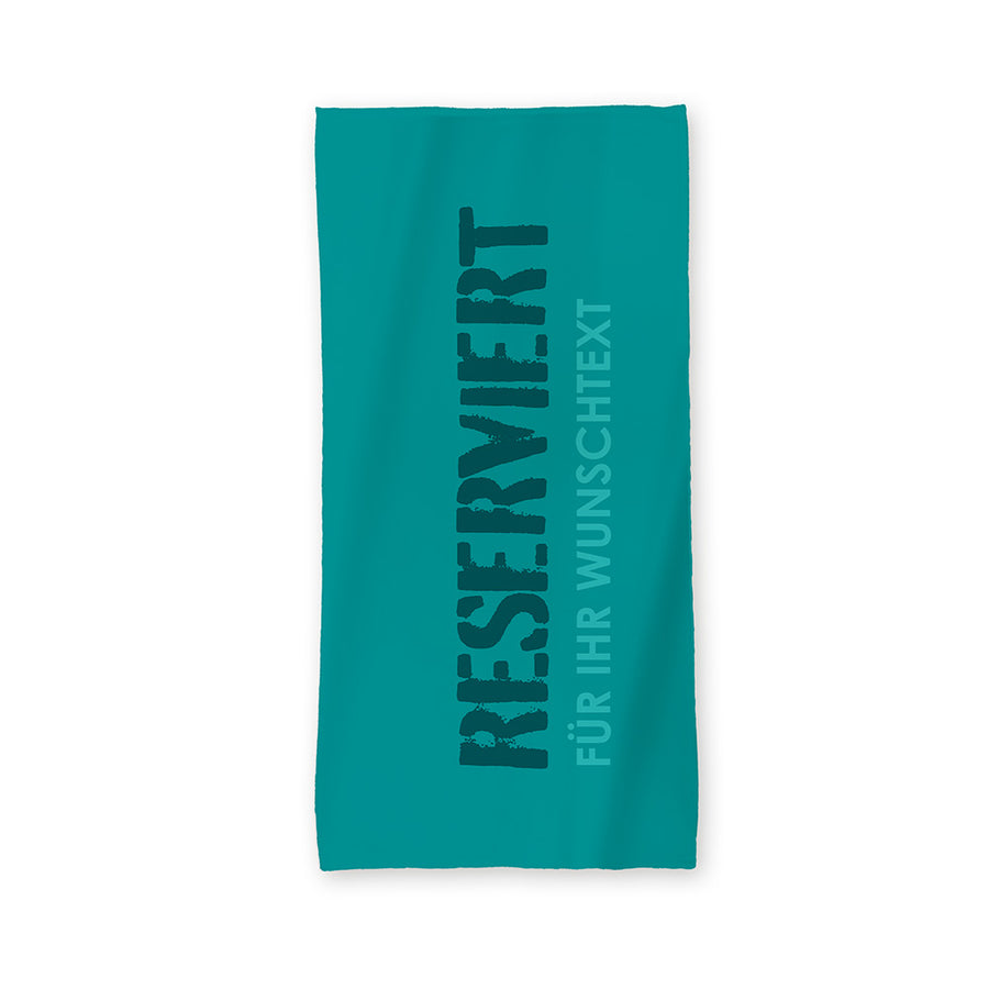Der Hintergrund des Handtuchs ist in einem helleren Petrol angelegt. Mittig steht in einer plakativen Schriftart "Reserviert". Darunter wird in einem helleren Farbton "FÜR IHR WUNSCHTEXT" abgebildet.
