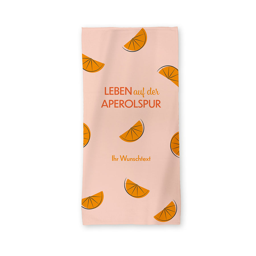 Helles Motiv mit dem Spruch "Leben auf der Aperolspur".  Auf dem Handtuch verteilt sind Orangenstücke.